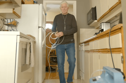 Man in kitchen holding chord from oxygen machine