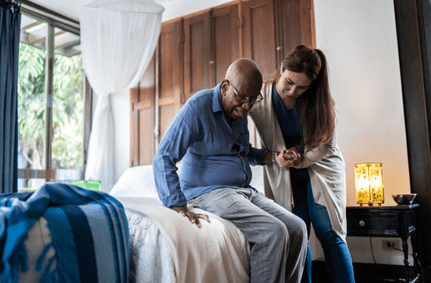 Caregiver helping male patient out of bed