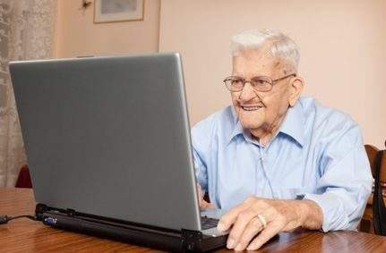 A smiling 90 year old man using a laptop computer.