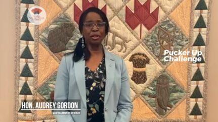 Honourable Audrey Gordon speaks in front of a Manitoban tapestry