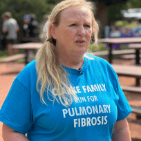 Woman standing in park looking at camera, wearing a blue PF tshirt.