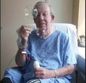 Man wearing hospital gown and oxygen blowing bubbles