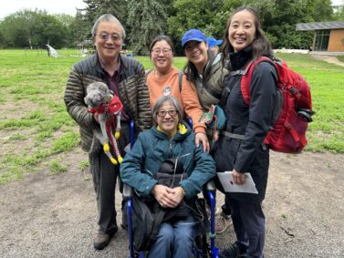 Family standing together behind family member in wheel chair in a park